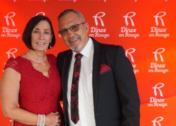 An image of a woman in a red dress with her arm around a men dressed in a black suit