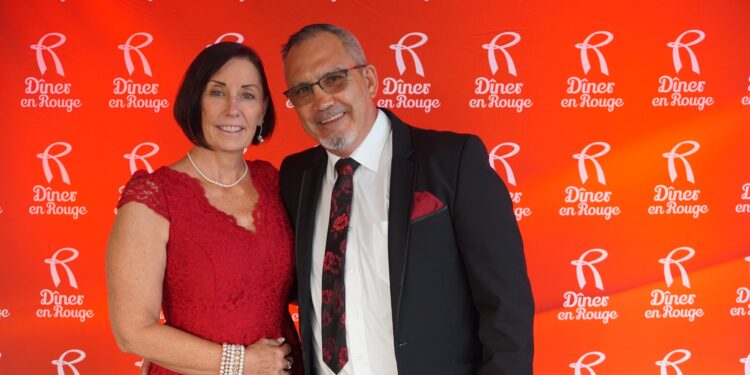 An image of a woman in a red dress with her arm around a men dressed in a black suit