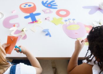 Two children sitting at a table making arts and crafts.