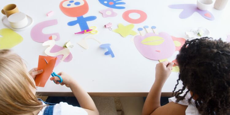 Two children sitting at a table making arts and crafts.